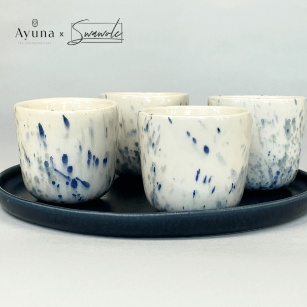 Vier Keramikbecher mit blauen Farbklecksen auf blauem Teller